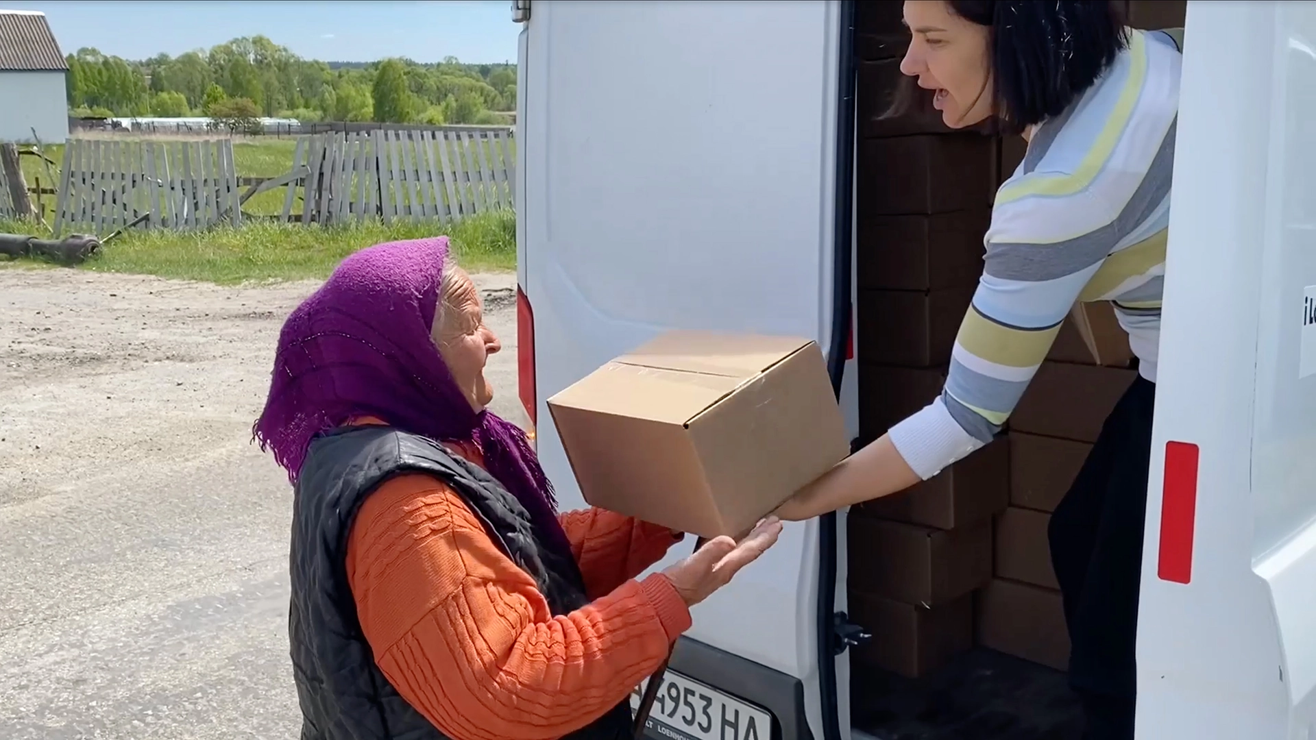 iLoveUkraine volunteer in Kyiv suburbs handing humanitarian aid package to a grandmother from a truck.